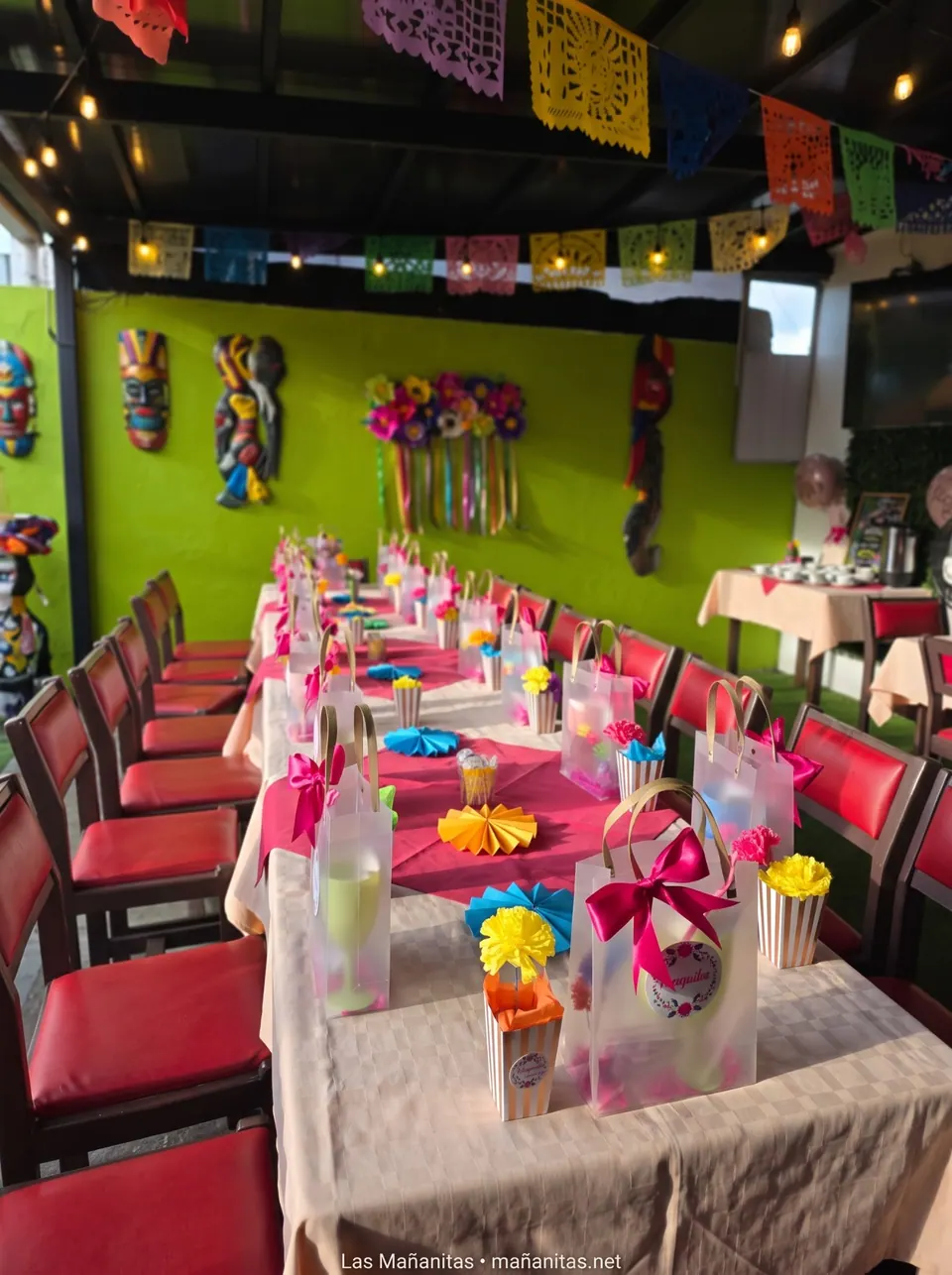Mesa de celebración con mantel rosado, lazos fucsia y abanicos de colores